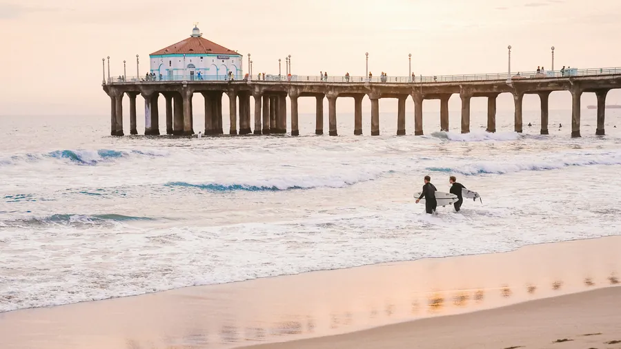 Surfers walking into the water beside the Manhattan Beach Pier
